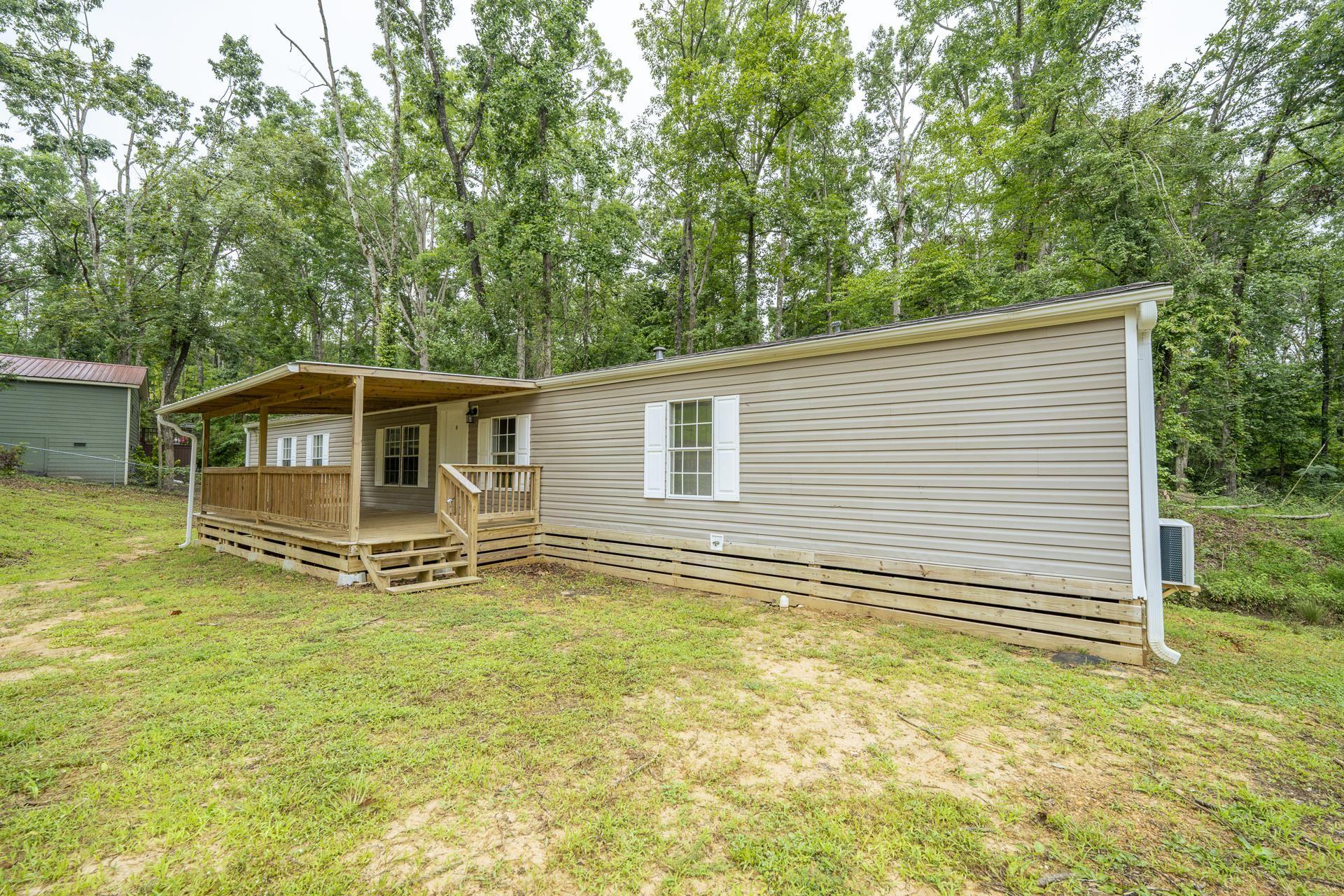 Image 3: Exterior featuring tan vinyl siding, white window shutters, and a covered wood deck