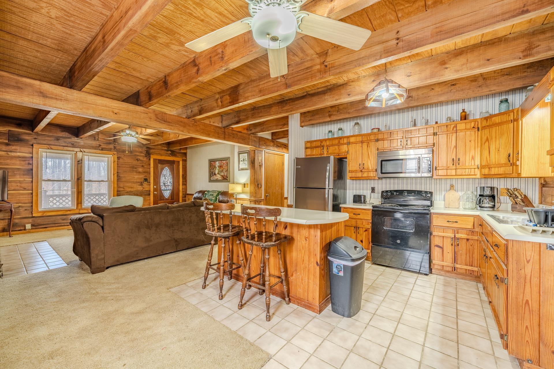 Image 2: Kitchen featuring wooden walls, light countertops, appliances with stainless steel finishes, a wooden ceiling with exposed beams, and a kitchen bar