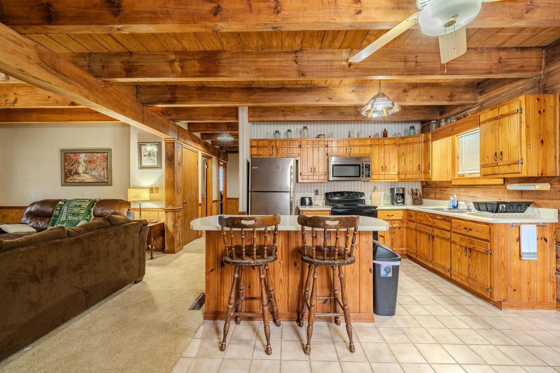 Image 3: Kitchen with a kitchen island, light countertops, appliances with stainless steel finishes, a kitchen breakfast bar, and a wood ceiling with exposed beams