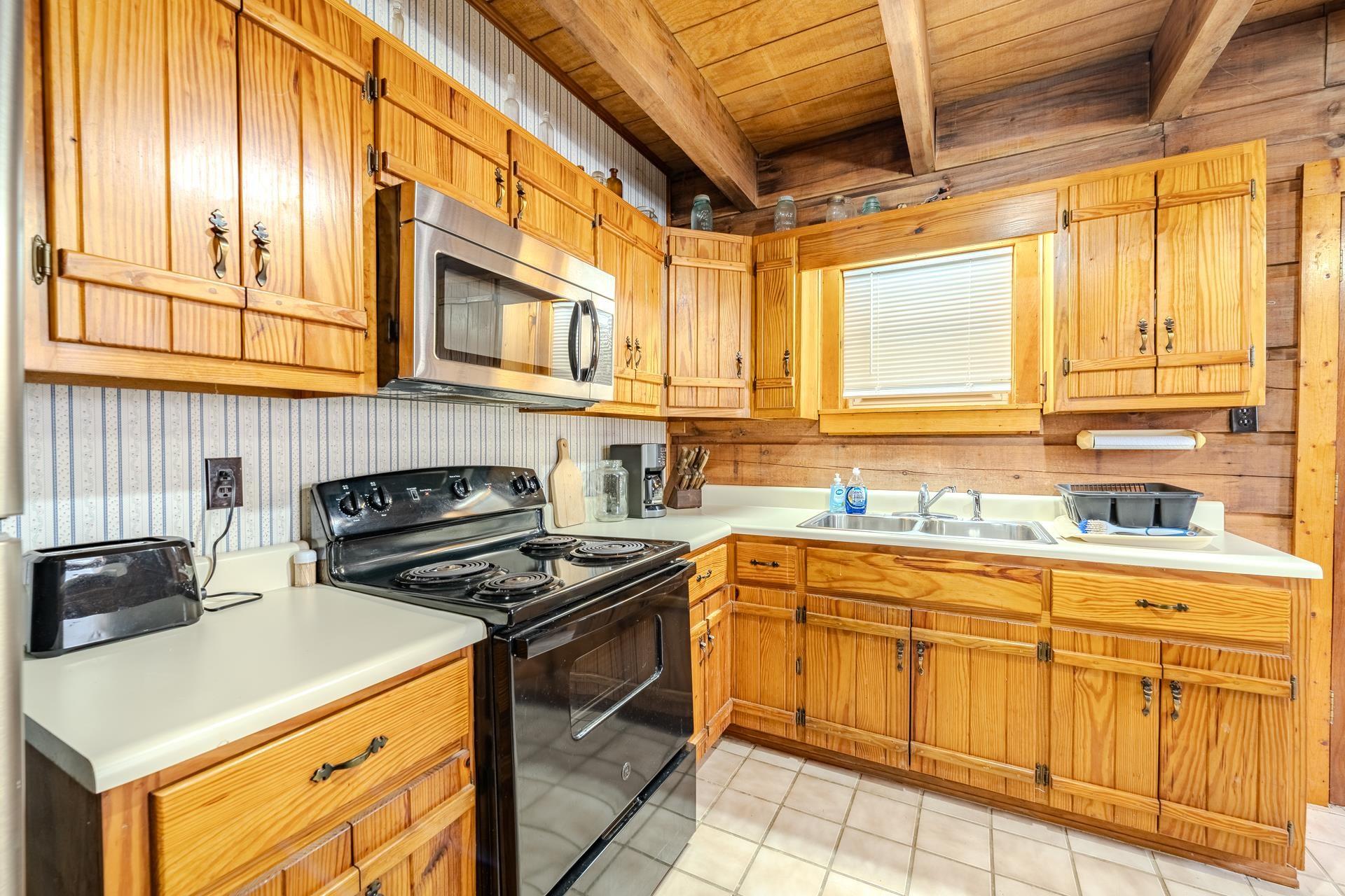 Image 4: Kitchen featuring black range with electric stovetop, stainless steel microwave, light countertops, a wood ceiling with exposed beams, and brown cabinetry