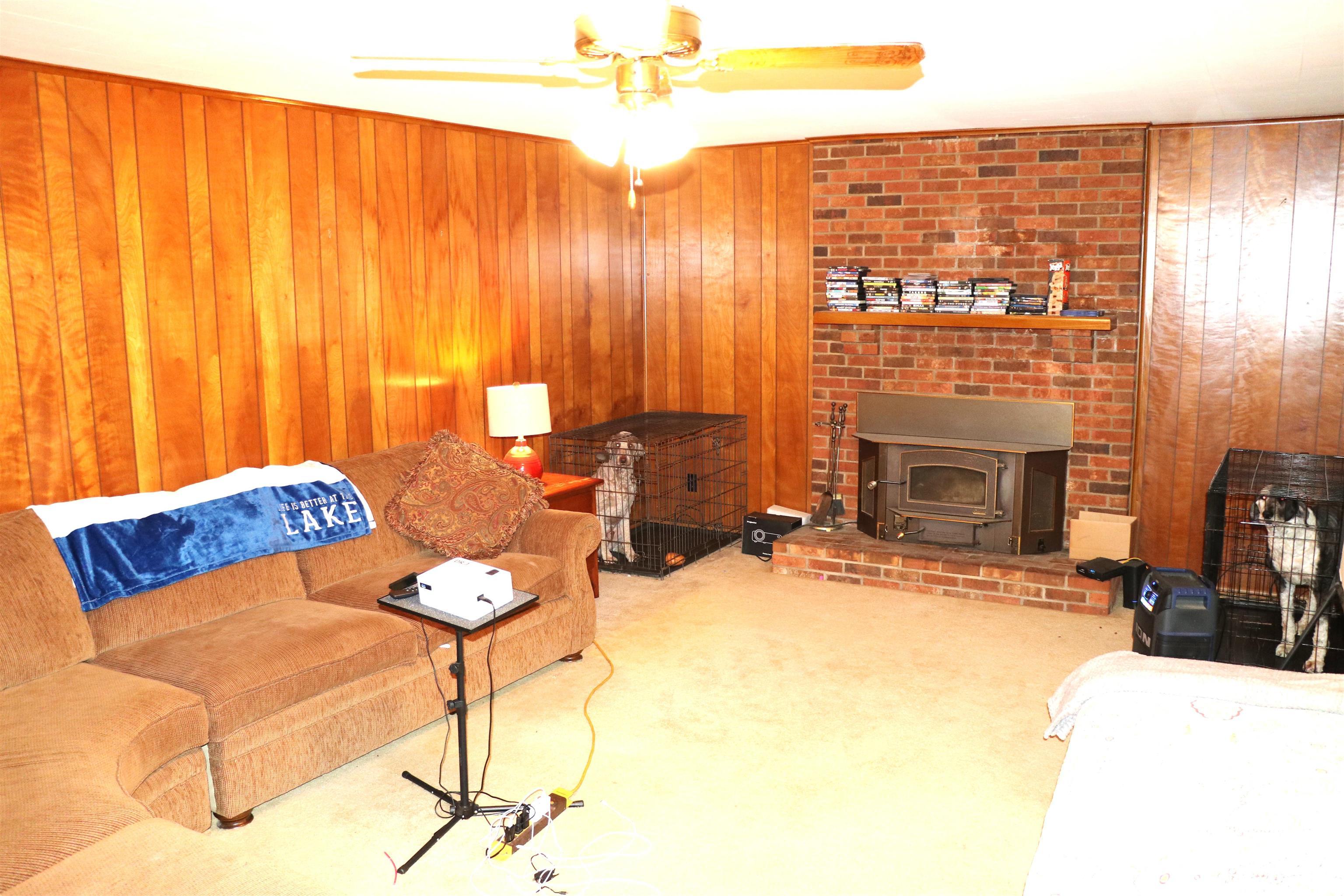 Image 2: Living area featuring wood paneling, a brick fireplace with a wood-burning insert, and a ceiling fan