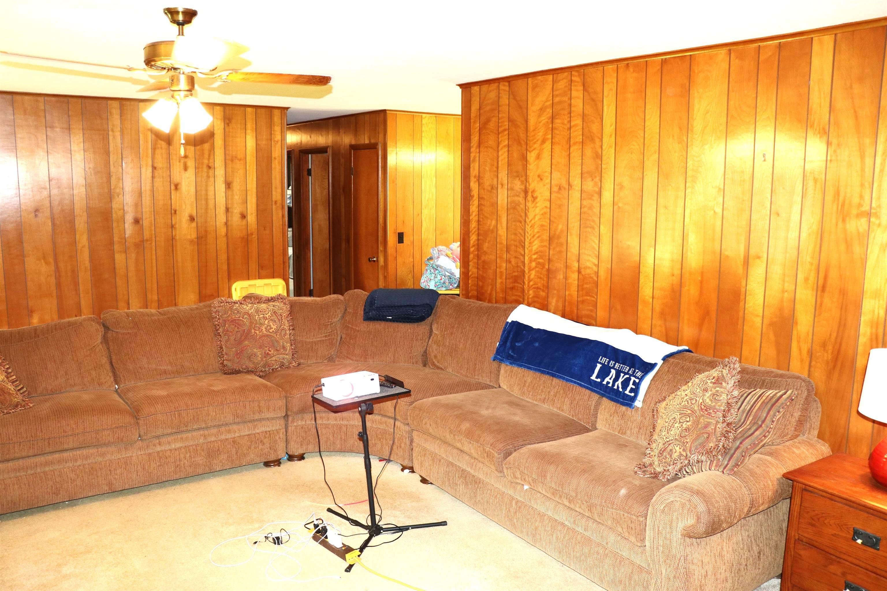 Image 3: Living area featuring wood paneling throughout, a ceiling fan with light fixture, and carpeted flooring