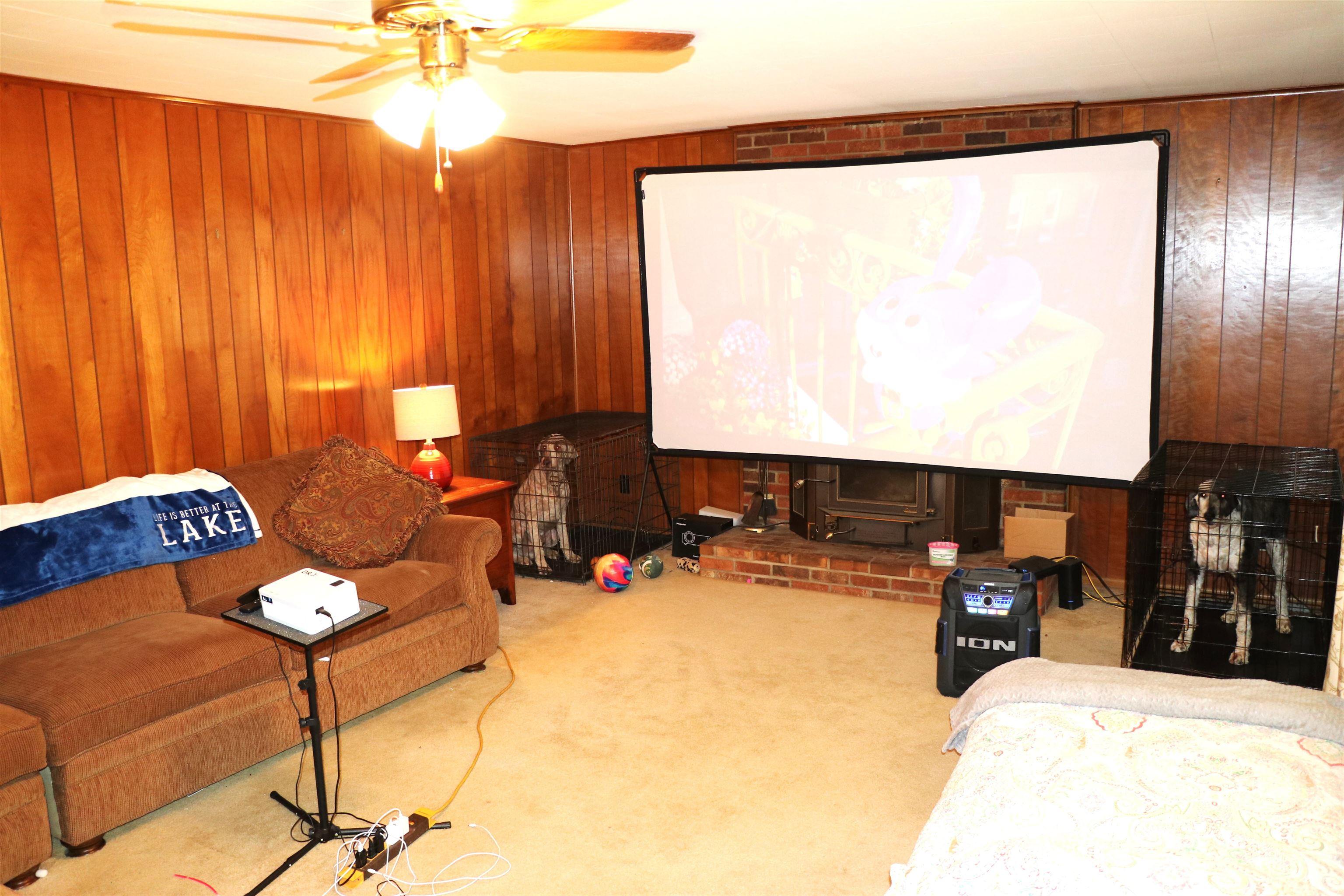 Image 4: Room featuring wood-paneled walls, carpet flooring, a ceiling fan with integrated lighting, and a brick fireplace hearth with a wood-burning stove insert