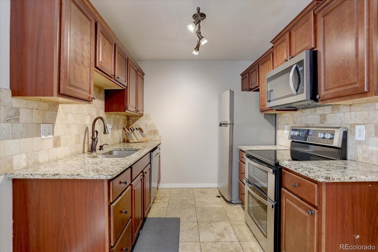 Image 1: Beautifully updated kitchen featuring stainless steel appliances, granite countertops, rich wood cabinetry, and a stylish tile backsplash for a warm and modern feel.