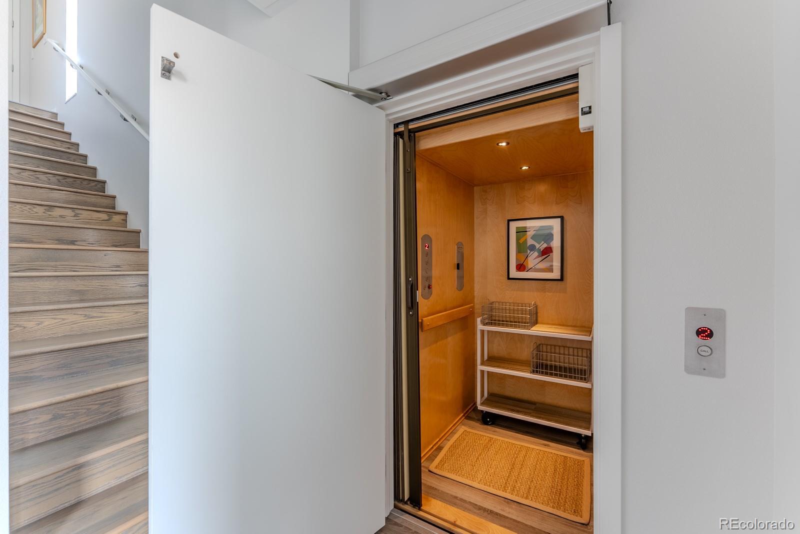 Image 3: Clean architectural lines, warm wood floors, and curated lighting create an artful first impression while the elevator spanning all levels and open staircase hint at the vertical refinement to come.