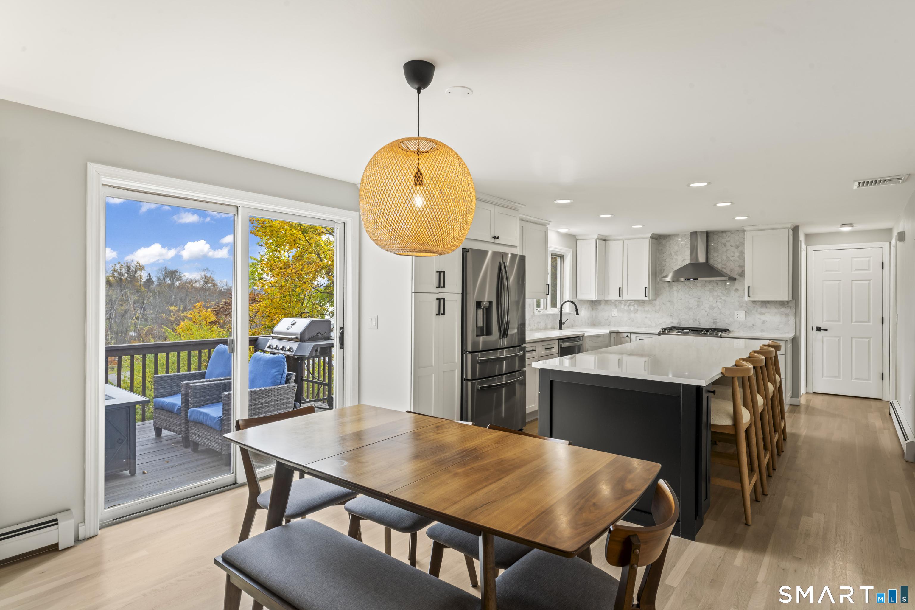 Image 3Dining Area: Spacious open-concept kitchen and dining area with seamless access to a private deck overlooking scenic lake and treetop views. Sliding glass doors fill the space with natural light and extend living outdoors, perfect for morning coffee or evening gatherings. The expansive center island, quartz countertops, custom cabinetry, and stainless steel appliances create a stylish and functional heart of the home. Designed for effortless entertaining and relaxed lake living.
