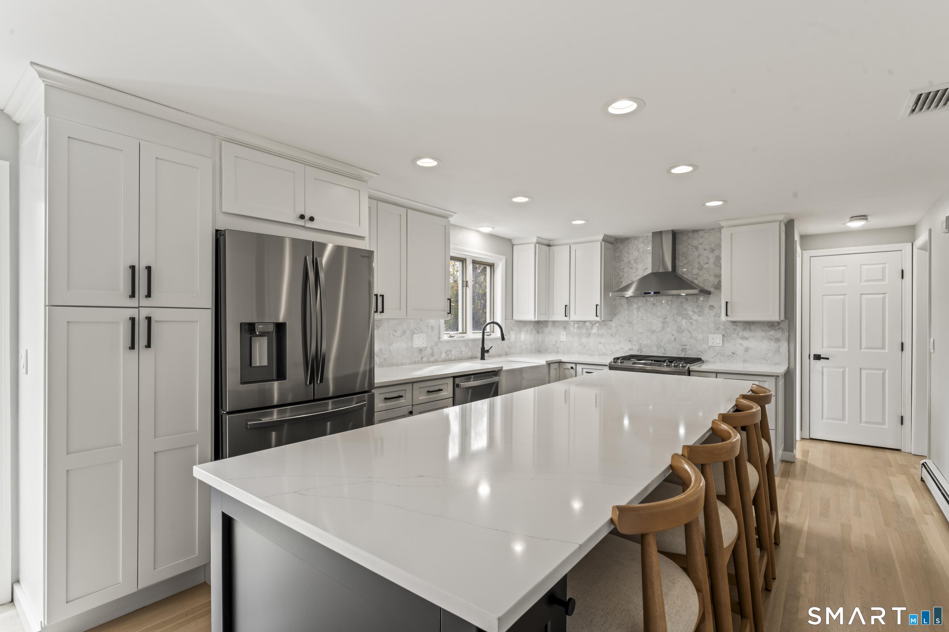 Image 4Island Kitchen: Stunning, fully renovated kitchen designed for both everyday living and entertaining. Features include custom white cabinetry, sleek quartz countertops, expansive center island with seating, and stainless steel appliances. Designer tile backsplash, modern vent hood, recessed lighting, and abundant storage enhance both style and function. A bright, open layout creates seamless flow, making this space the true heart of the home.