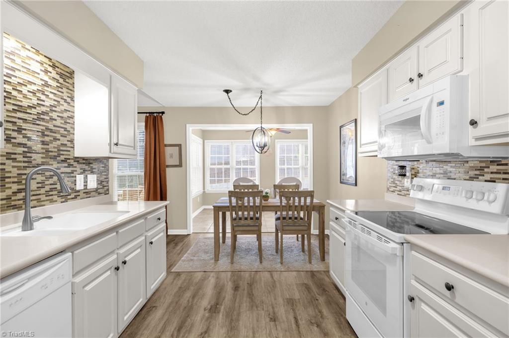 Image 3: A bright, well-designed kitchen featuring white cabinetry, updated tile backsplash, and warm wood-tone flooring. The layout opens into a cozy breakfast area and a sun-filled sitting room, creating an inviting space for meals and gatherings.
