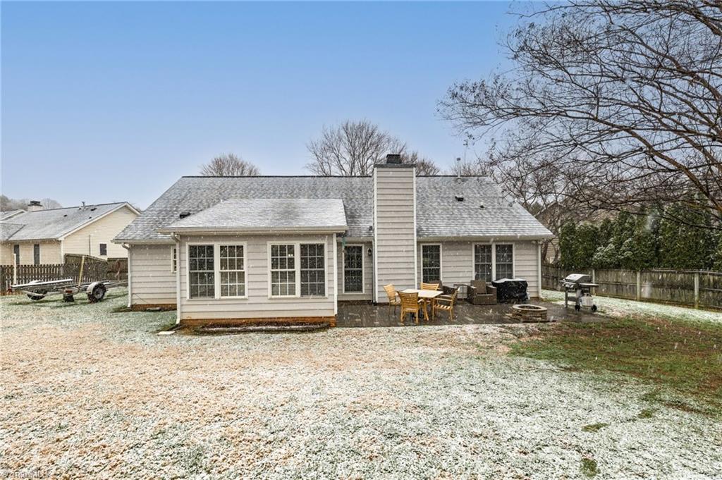 Image 4: A full rear view of the home showcasing the sunroom, spacious patio, and lightly snow-covered yard. The fenced outdoor area offers ample room for activities while maintaining a peaceful, private setting.