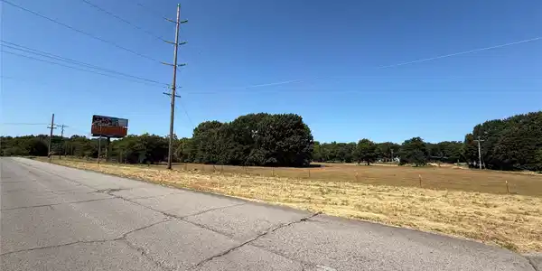 Image 2: Expansive open field with scattered trees and a cl