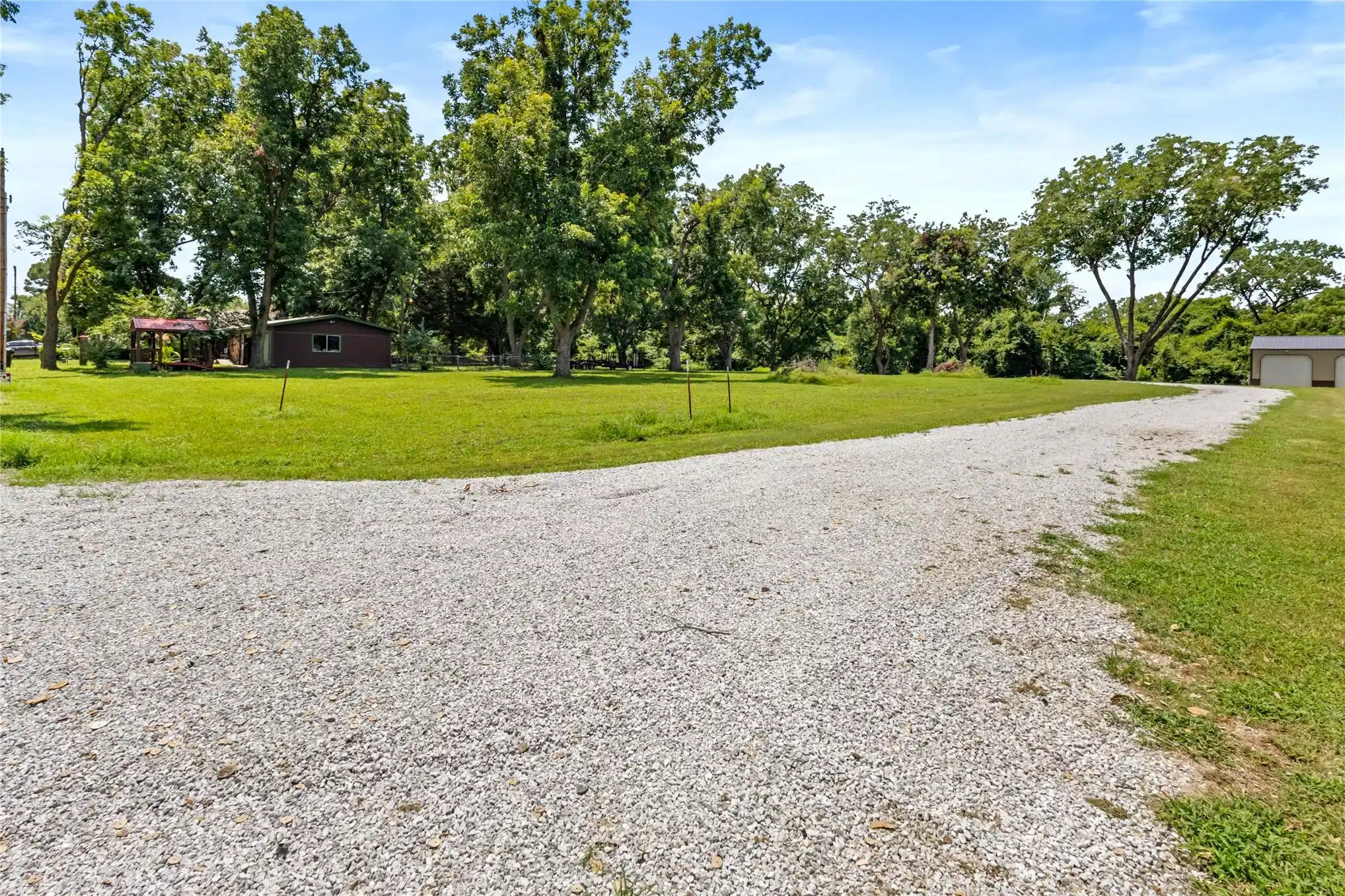 Image 1: Spacious gravel driveway leading to a verdant land
