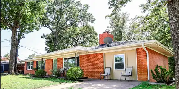 Image 2: Brick facade ranch home featuring mature trees, a