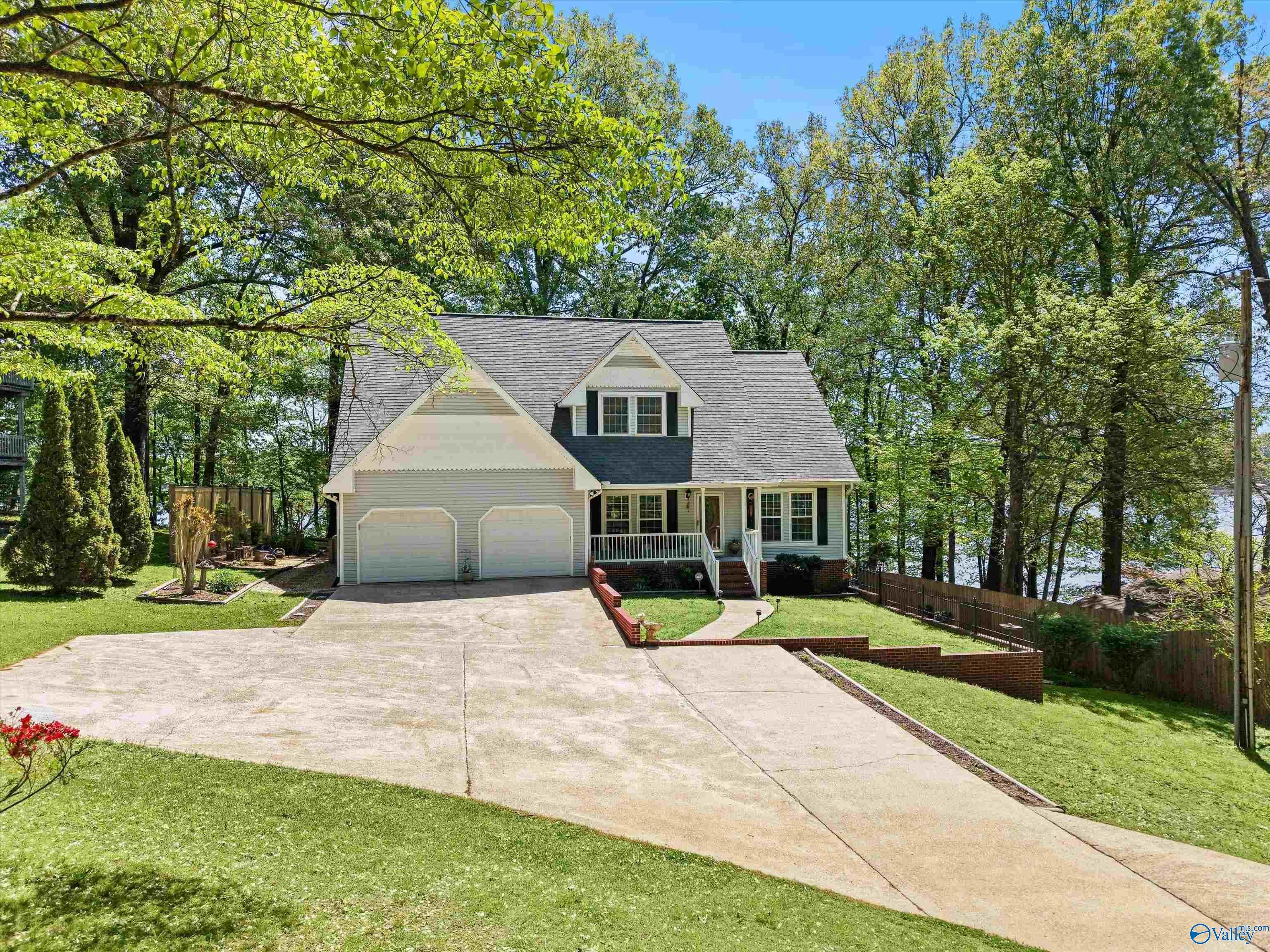 Image 1: Vinyl house, concrete driveway and sidewalks, covered front porch with railing and home entry, two car attached garage, shaded yard beautifully maintained yard