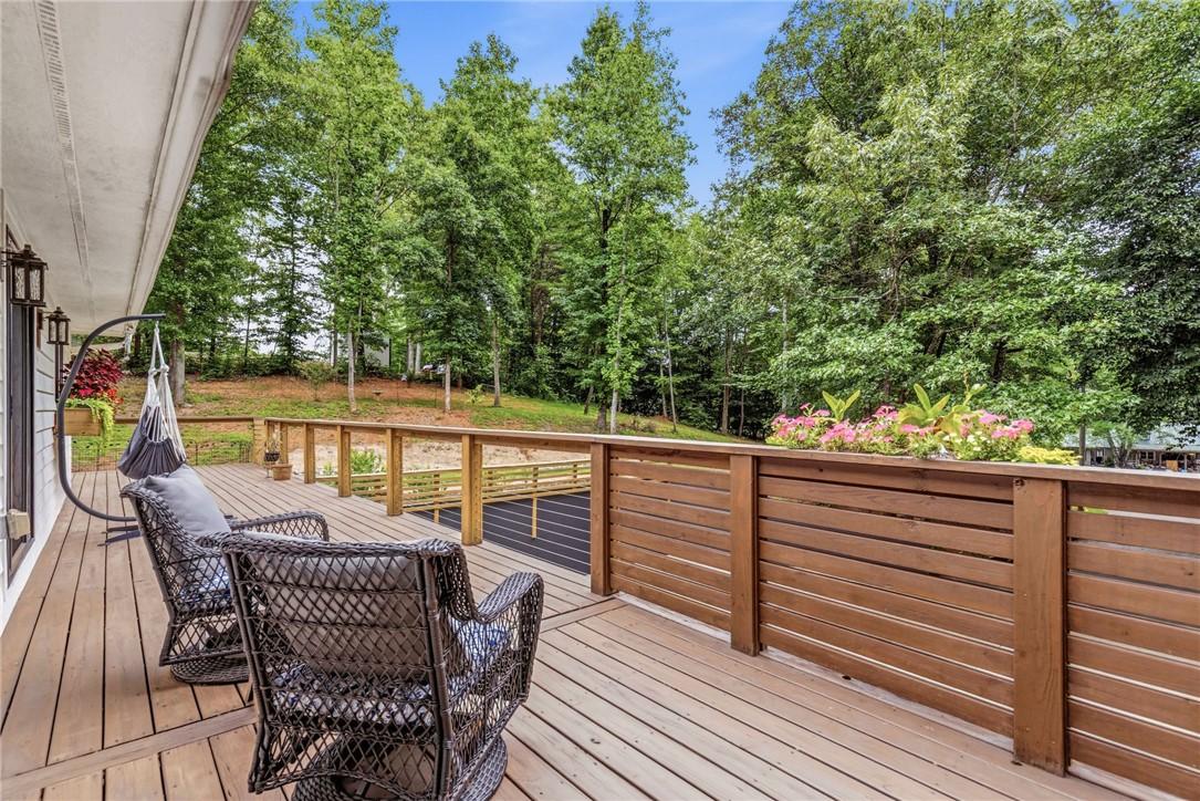 Image 4: A spacious wooden deck extends into a lush, wooded